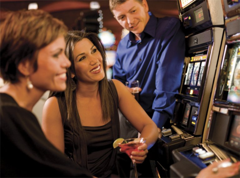 Ein Mädchen sitzt am Spielautomaten, und ihre Freunde sehen ihr beim Spielen zu